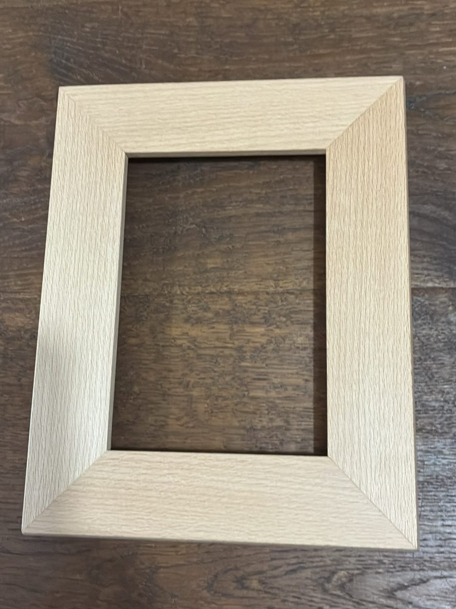 A pale, wide-profile wood picture frame seen from directly above on a dark oak table.