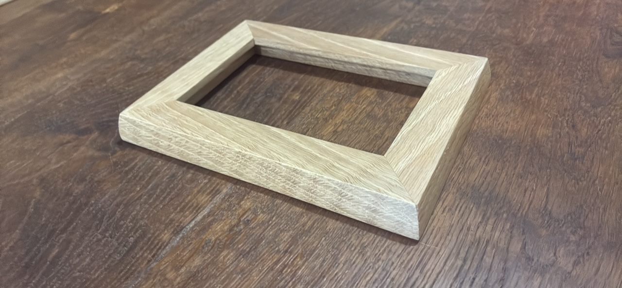 Low angle view of an oak picture frame on a dark table, showing its depth and tight mitered corners.