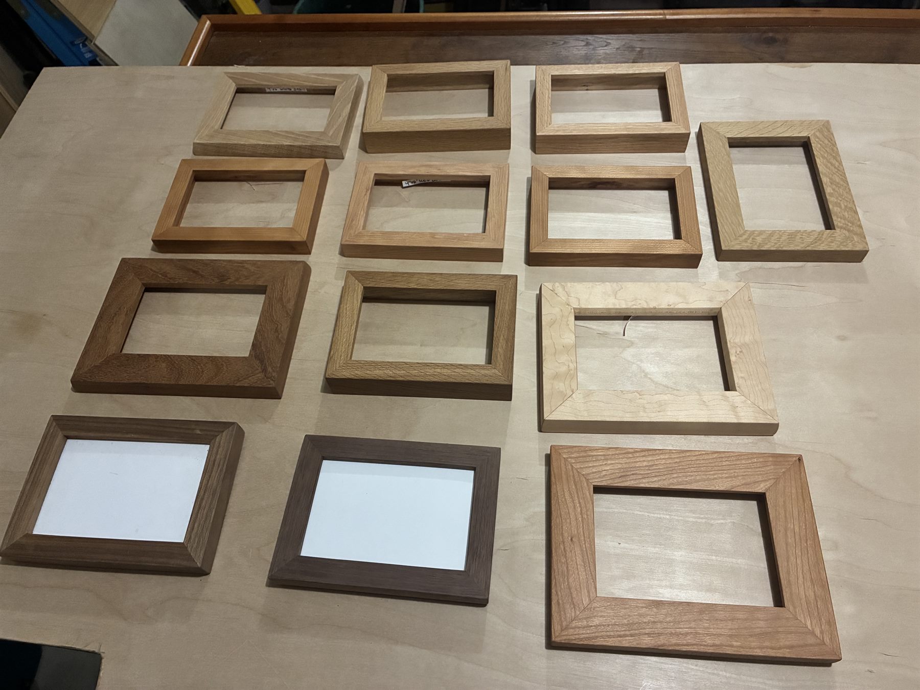More than a dozen handmade wood picture frames in oak, walnut, cherry and maple laid out on a workbench.