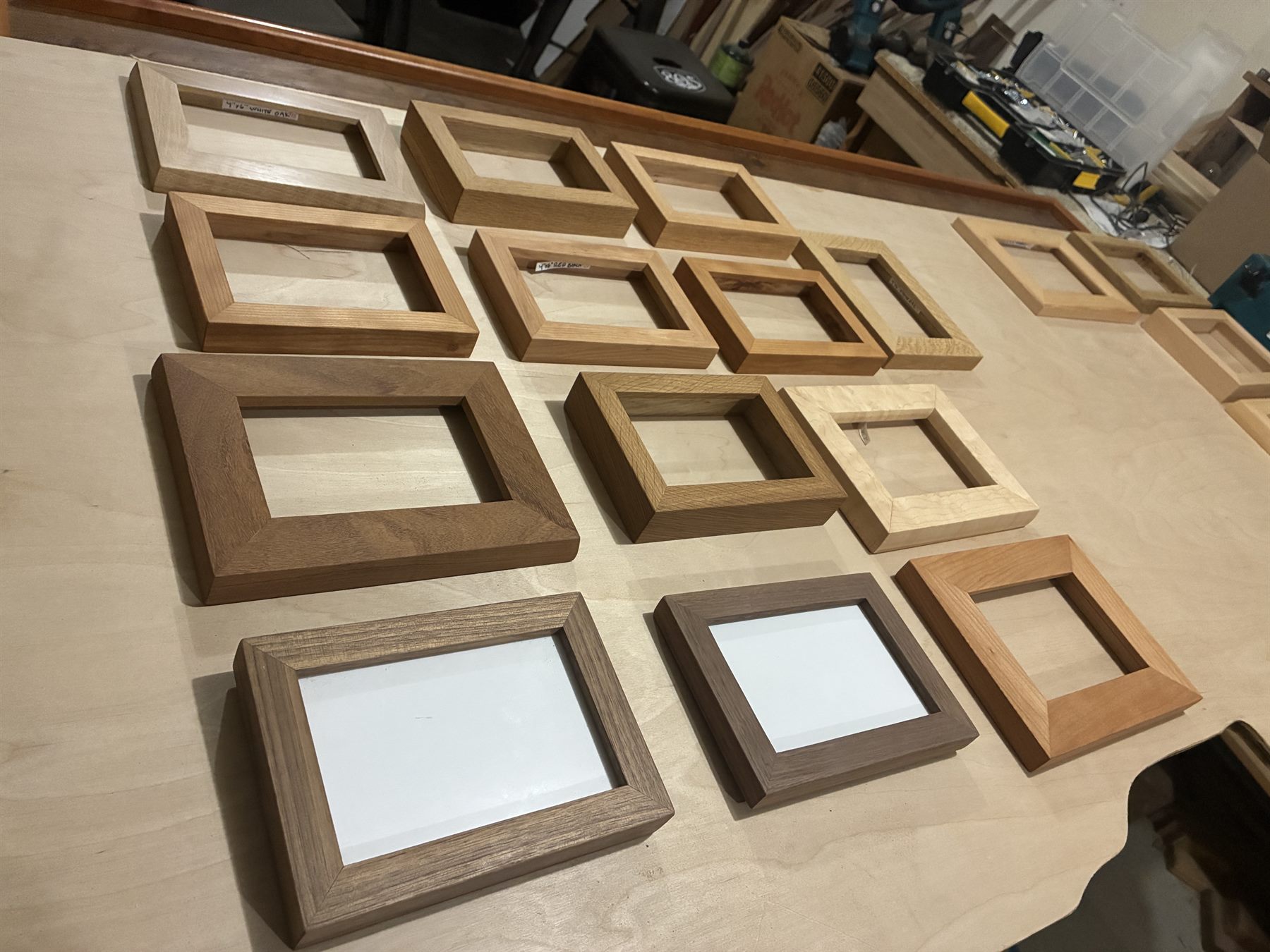 A workbench in Adam's shop covered with finished frames, tool cases and offcuts stacked behind.