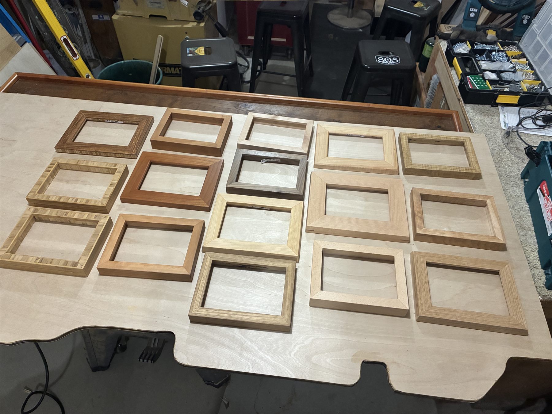 Fifteen frames laid out in a grid on a workbench, in bamboo, purpleheart, oak and birch.